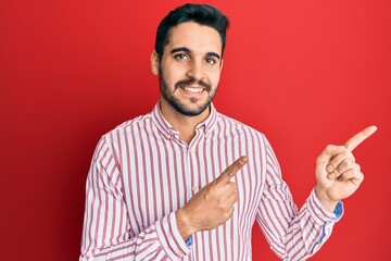 Fototapeta premium Young hispanic man wearing business shirt smiling and looking at the camera pointing with two hands and fingers to the side.