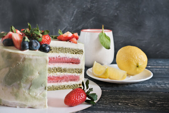 layered matcha and strawberry cake and a cup of tea with lemon and mint. birthday selebration. holiday food. vegetarian homemade cake with superfood ingredients.