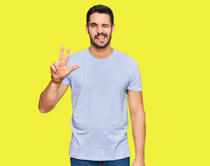 Young hispanic man wearing casual clothes smiling with happy face winking at the camera doing victory sign with fingers. number two.
