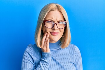 Fototapeta premium Young blonde woman wearing casual clothes and glasses touching mouth with hand with painful expression because of toothache or dental illness on teeth. dentist