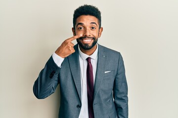 Handsome hispanic man with beard wearing business suit and tie pointing with hand finger to face and nose, smiling cheerful. beauty concept