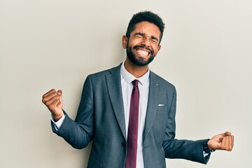 Handsome hispanic man with beard wearing business suit and tie very happy and excited doing winner...