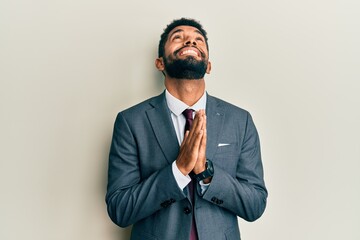 Handsome hispanic man with beard wearing business suit and tie begging and praying with hands together with hope expression on face very emotional and worried. begging.