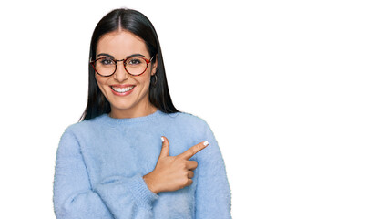 Young hispanic woman wearing casual clothes and glasses cheerful with a smile of face pointing with...