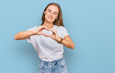 Beautiful young blonde woman wearing casual white t shirt smiling in love doing heart symbol shape with hands. romantic concept.