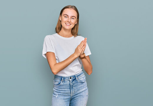 Beautiful young blonde woman wearing casual white t shirt clapping and applauding happy and joyful, smiling proud hands together