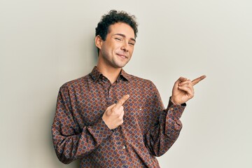 Handsome hispanic man wearing casual clothes smiling and looking at the camera pointing with two hands and fingers to the side.