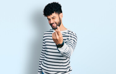 Young arab man with beard wearing casual striped sweater beckoning come here gesture with hand inviting welcoming happy and smiling