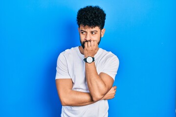 Young arab man with beard wearing casual white t shirt looking stressed and nervous with hands on mouth biting nails. anxiety problem.