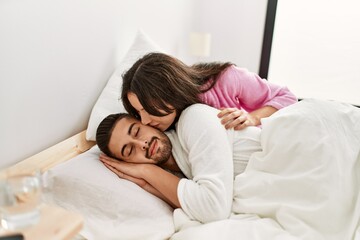 Young hispanic woman kissing her sleepy boyfriend at bed.