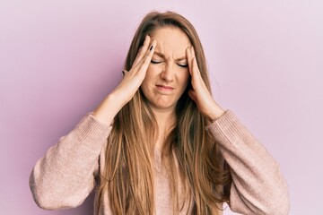 Young blonde woman wearing casual sweater suffering from headache desperate and stressed because pain and migraine. hands on head.