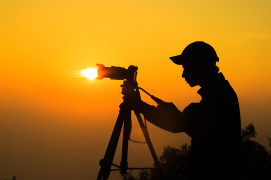 Silhouette of a young photographer, taking pictures of the landscape at sunset