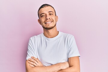 Hispanic young man wearing casual white t shirt happy face smiling with crossed arms looking at the camera. positive person.