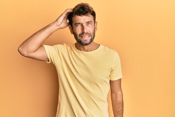 Handsome man with beard wearing casual yellow tshirt over yellow background confuse and wonder...