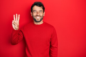 Handsome man with beard wearing casual red sweater showing and pointing up with fingers number...