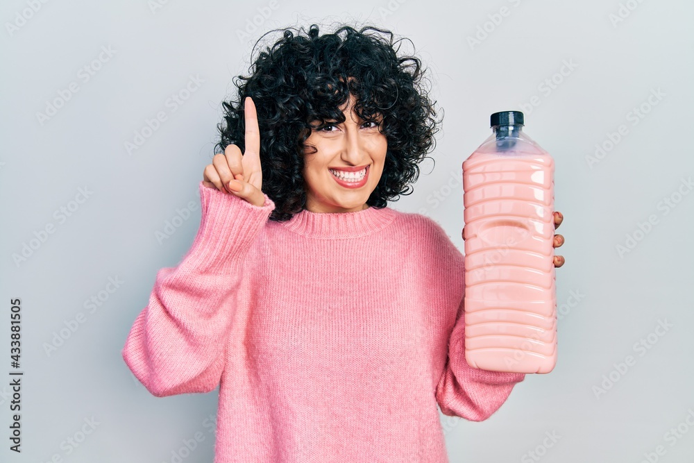 Sticker Young middle east woman holding detergent bottle smiling with an idea or question pointing finger with happy face, number one