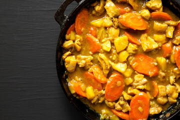 Homemade Japanese Chicken Curry in a cast-iron pan on a black background, top view. Flat lay, overhead, from above. Space for text.