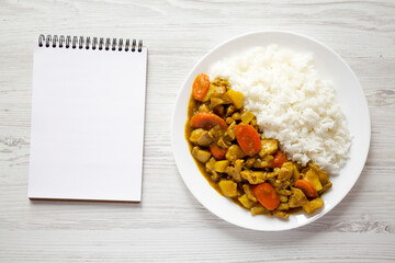 Homemade Japanese Chicken Curry  on a white plate on a white wooden background, blank notepad, top view. Flat lay, overhead, from above.