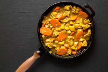 Homemade Japanese Chicken Curry in a cast-iron pan on a black background, top view. Flat lay, overhead, from above. Copy space.