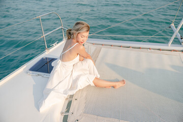 Woman wearing white dress relax on sailing yacht, romantic sunset.