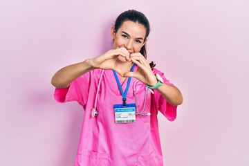 Young brunette woman wearing doctor uniform and stethoscope smiling in love doing heart symbol...