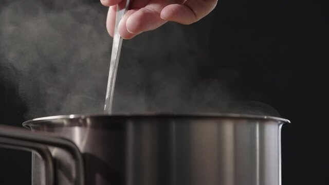 Slow motion man hand stiring with fork in saucepan with rising steam