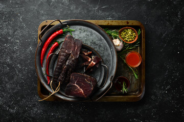 Dried veal beef with spices and herbs. On a black stone background. Top view. Free space for text.