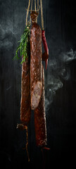 Delicious salami sausage with spices and rosemary. On a black stone background. Top view. Free space for text.