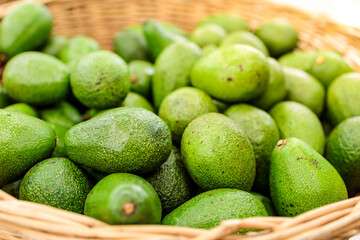 juicy green avocados lie in a wooden basket, close-up, blurry