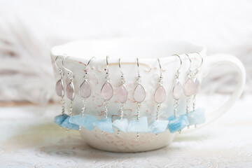 Fototapeta na wymiar Decorative white cup with many stone mineral earrings on white background