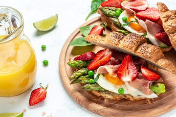 Breakfast, business lunch sandwiches Croissant with avocado, asparagus, jamon, ham, prosciutto, strawberries, sunny side up eggs and juice, Food recipe background. Close up