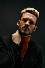 Obraz premium fashionable blond man in a sweater and a jacket on a dark background tilted his head to the side 