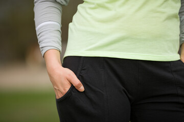 Close-up of the athletic body of a woman in sweatpants and a sweatshirt on a green background. The concept of sports and a healthy lifestyle.