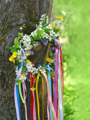 Spring flower wreath with colorful ribbons in garden. floral traditional decor. Symbol of Beltane,...