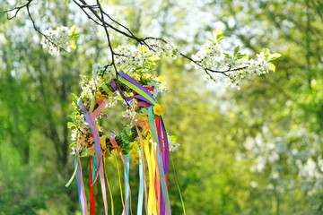 Spring flower wreath with colorful ribbons in garden. floral traditional decor. Symbol of Beltane, Wiccan Celtic Holiday beginning of summer. wheel of the year, pagan witch traditions and rituals - obrazy, fototapety, plakaty