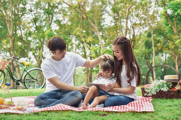Portrait of happy Asian family, parents and daughter enjoying picnic meal in garden.Asian, Asian...
