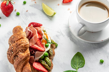 Breakfast, business lunch sandwiches Croissant with avocado, asparagus, jamon, ham, prosciutto, strawberries, sunny side up eggs, coffee, Food recipe background