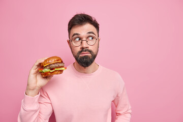 Fast food concept. Hungry bearded man holds appetizing hamburger going to have unhealthy delicious...