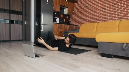 Man training on mat with laptop at home, doing bicycle exercise on back