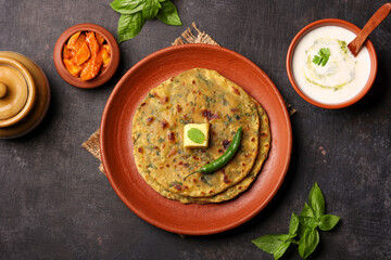 Palak paratha butter on spinach paratha , parantha ,chapati Indian flatbread roti made from spinach served in golden plate with yogurt mint dip, mango pickle, North Indian breakfast food Delhi India.