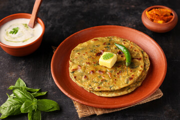 Palak paratha butter on spinach paratha , parantha ,chapati Indian flatbread roti made from spinach served in golden plate with yogurt mint dip, mango pickle, North Indian breakfast food Delhi India.