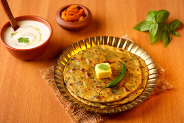 Palak paratha butter on spinach paratha , parantha ,chapati Indian flatbread roti made from spinach served in golden plate with yogurt mint dip, mango pickle, North Indian breakfast food Delhi India.