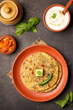 Palak paratha butter on spinach paratha , parantha ,chapati Indian flatbread roti made from spinach served in golden plate with yogurt mint dip, mango pickle, North Indian breakfast food Delhi India.
