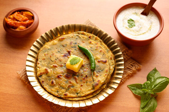 Palak paratha butter on spinach paratha , parantha ,chapati Indian flatbread roti made from spinach served in golden plate with yogurt mint dip, mango pickle, North Indian breakfast food Delhi India.