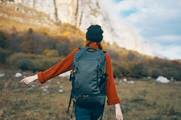 woman in a warm hat with a backpack on her back and in a sweater outdoors in the mountains gesticulate with her hands