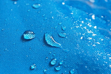 Closeup of water drops on bright blue fabric with waterproof design to protect fabric of the cloth...