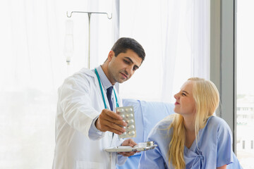 Fototapeta premium Focus on the medicine panel held by a male doctor introducing a female patient to sit on bed