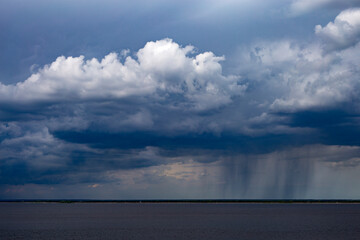 Obraz premium Rainy clouds over the river. Dark cloud in rainy weather over the river. Storm clouds over horizon. Stormy sky over the river. Dramatic weather