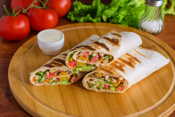 delicious shawarma lavash wrap with chicken meat tomatoes lettuce cucumber  potato sauce bowl on cutting board  close up