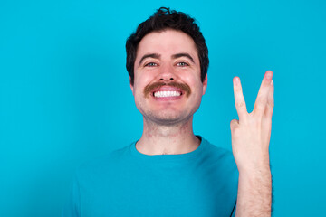 young handsome Caucasian man with moustache wearing blue t-shirt against blue background smiling...